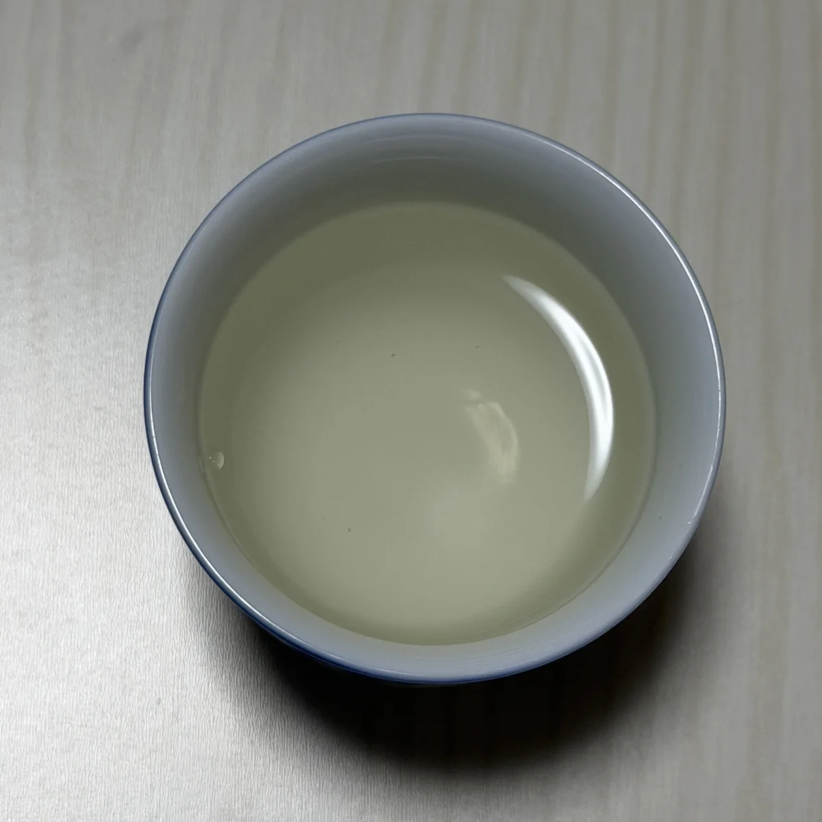Amabuki hiyaoroshi seen from above in a white porcelain cup, showing its faint pale yellow tint