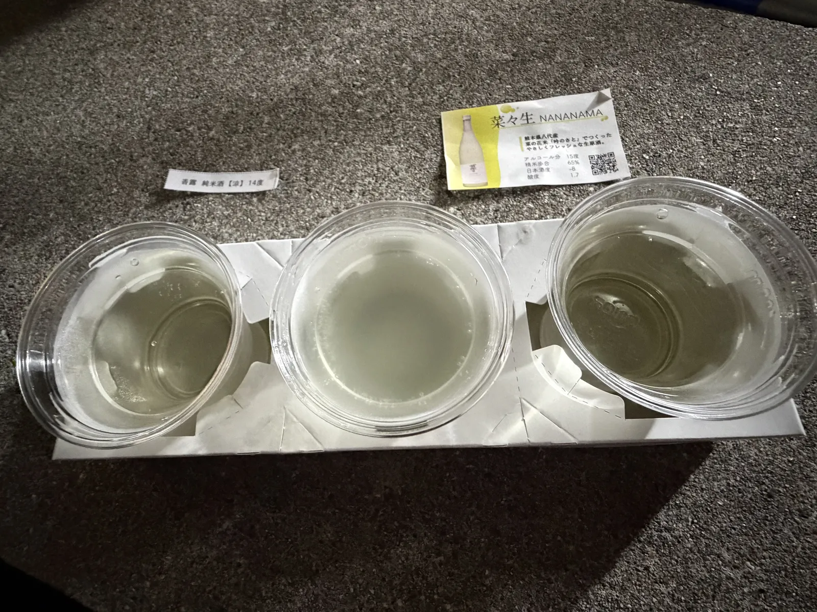 Three cups of sake in a cardboard holder with the festival behind