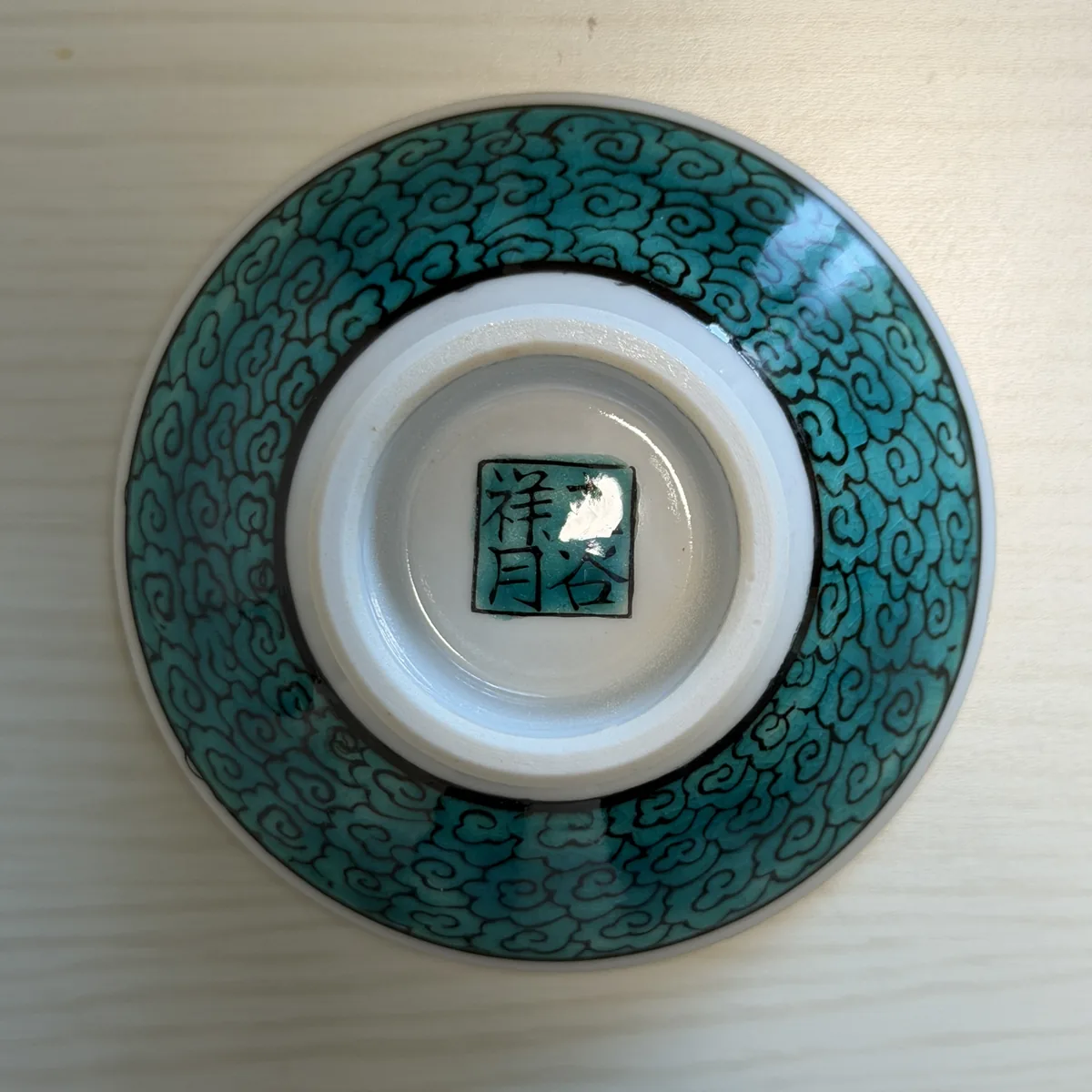 Underside of the Kutani ware sakazuki, covered in turquoise scroll patterns with a square mark in the center of the foot