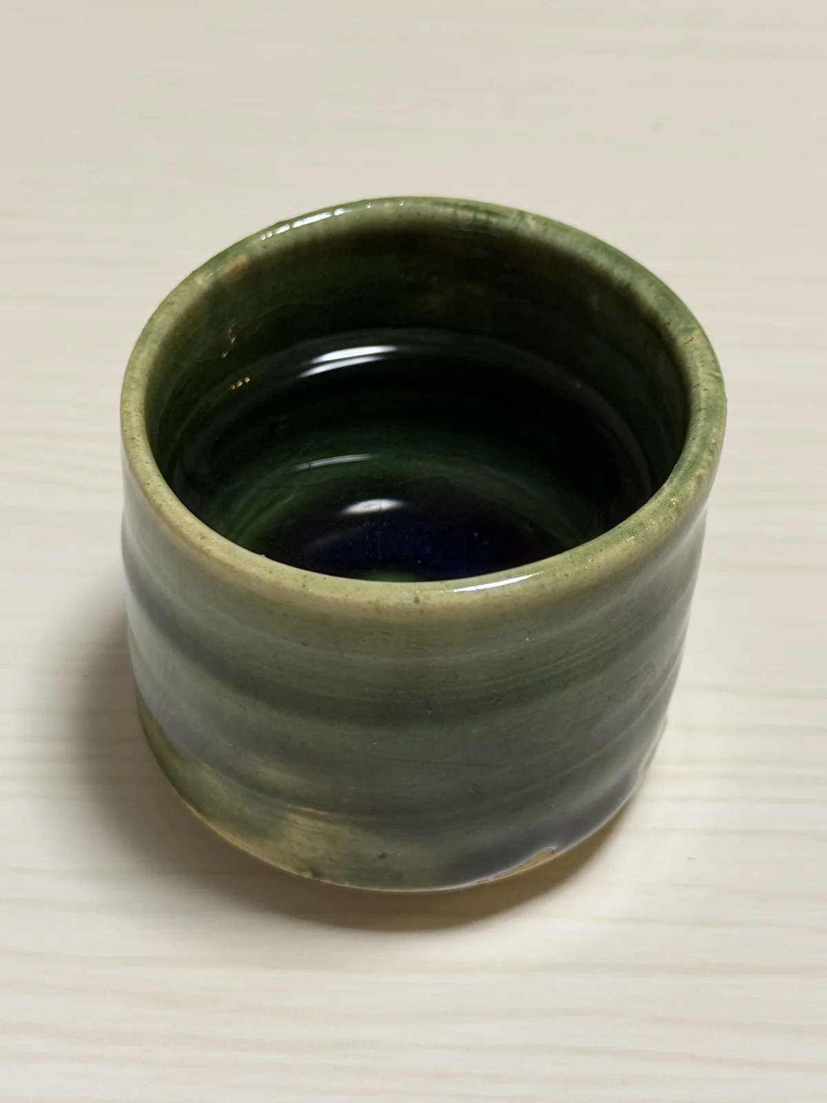 Oribe ware guinomi seen from above, its dark green glossy interior reflecting light